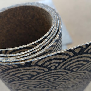 May include: A roll of cork fabric with a black and beige wave pattern. The fabric is rolled up tightly and the pattern is visible on the outside of the roll.