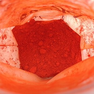 May include: A close-up view inside a white paper bag filled with a bright orange powder. The powder is piled high in the center of the bag.