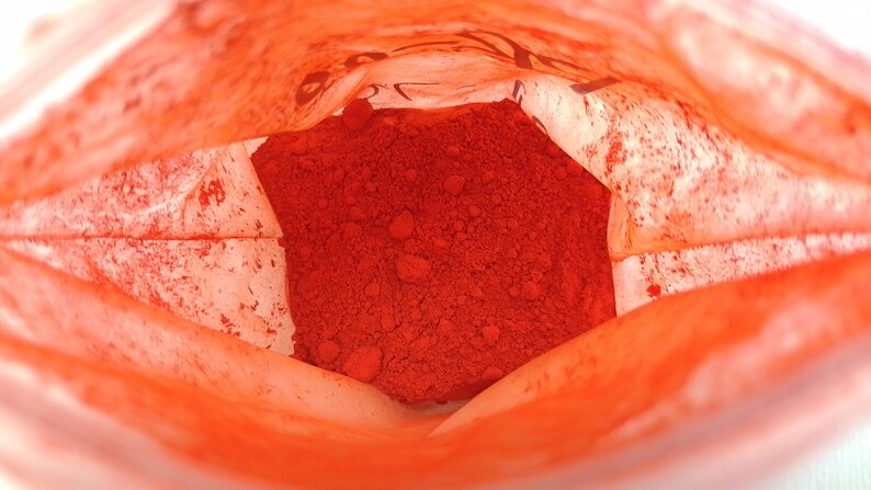 May include: A close-up view inside a white paper bag filled with a bright orange powder. The powder is piled high in the center of the bag.