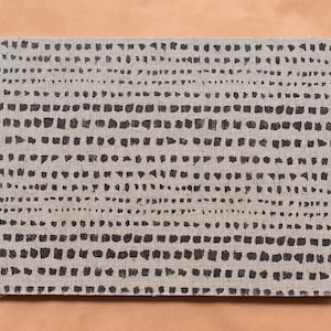 May include: Rectangular beige mousepad with a repeating pattern of black, unevenly spaced dots arranged in horizontal rows. The mousepad has rounded corners and is set against a light brown background.