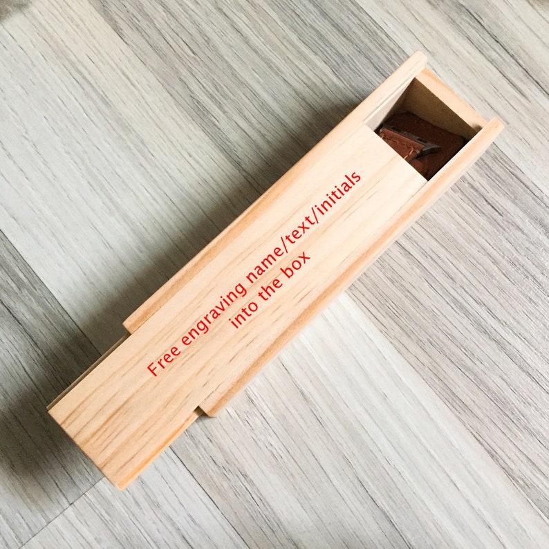 Puede incluir: Una caja de madera con tapa deslizante. La caja es de color marr&oacute;n claro y tiene el texto "Free engraving name/text/initials into the box" impreso en rojo en el lateral.
