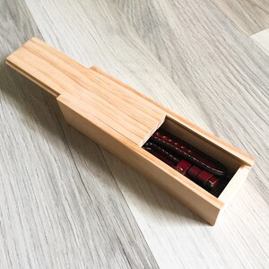 Puede incluir: Una caja de madera con una tapa deslizante, que revela dos correas de reloj de cuero marr&oacute;n en el interior.