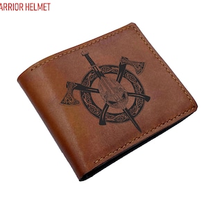 Puede incluir: Una cartera plegable de cuero marrón con un diseño grabado con láser en negro de un casco de guerrero vikingo centrado en un patrón de nudo celta circular, flanqueado por dos hachas cruzadas. El texto VIKING WARRIOR HELMET aparece en rojo.