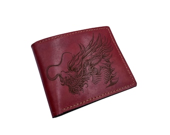 Op de afbeelding: Een donkerrode bifold portemonnee met een gedetailleerde, donker gegraveerde drakenillustratie op de voorkant. De portemonnee is voorzien van zichtbare stiksels langs de randen en heeft een gladde, matte afwerking en een klassieke vorm.