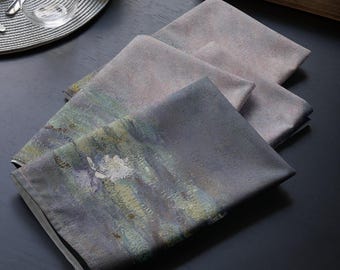 Op de afbeelding: Vier gevouwen stoffen servetten met een abstract aquarelontwerp in grijstinten, blauw, groen en wit.
