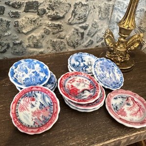 May include: A set of miniature blue and white and red and white porcelain plates with a floral design. The plates are stacked on a wooden table.