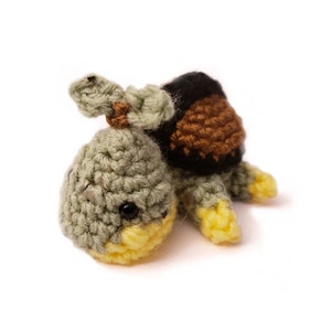May include: A small crocheted turtle toy with a green body, brown shell, and yellow feet. The turtle has black eyes and a small, brown nose.
