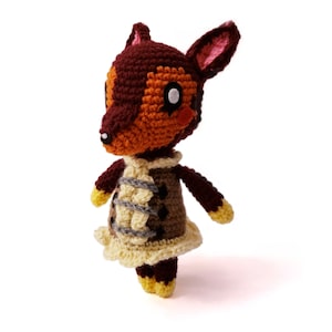 Puede incluir: Un juguete de peluche de crochet marrón y naranja con un vestido amarillo y marrón. El juguete tiene una cara blanca con ojos negros y una nariz rosa.