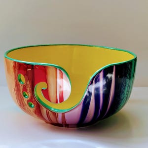 May include: A colourful yarn bowl with a green rim and a swirl design in shades of red, orange, yellow, purple, and blue.