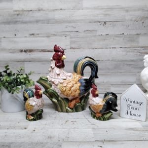 May include: A ceramic rooster-shaped teapot and two matching rooster-shaped shakers. The pieces feature a glossy finish with red, yellow, blue, and green colors. A white house-shaped sign with the text Vintage Tenn House is included.