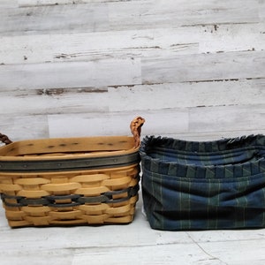 May include: Two storage baskets. The first is a rectangular woven basket with a light brown and grey design, brown braided handles, and a dark grey trim. The second is a blue and green plaid fabric basket.
