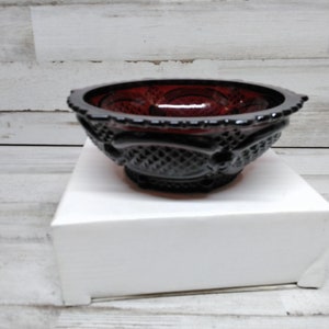 May include: A small, dark red glass bowl with a decorative pattern. The bowl is sitting on a white surface.