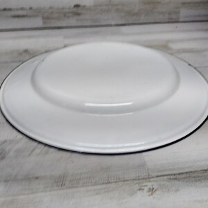 Peut inclure: Assiette plate en &eacute;mail blanc avec un bord noir. L'assiette est ronde et a un bord l&eacute;g&egrave;rement sur&eacute;lev&eacute;.