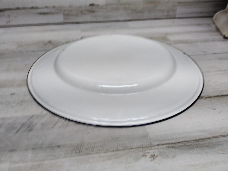 Peut inclure: Assiette plate en &eacute;mail blanc avec un bord noir. L'assiette est ronde et a un bord l&eacute;g&egrave;rement sur&eacute;lev&eacute;.