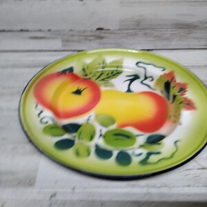 Peut inclure: Une assiette en &eacute;mail vintage avec un bord vert et un centre blanc. L'assiette pr&eacute;sente un motif peint &agrave; la main de pommes rouges et jaunes avec des feuilles vertes.