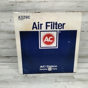 Peut inclure: Boîte blanche et bleue pour un filtre à air AC Delco. La boîte porte l'inscription "Air Filter" en grandes lettres noires en gras. Le logo AC est dans un cercle rouge avec du texte blanc. La boîte porte également l'inscription "AC-Delco Genuine GM Parts".