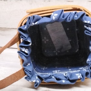 May include: A small, brown wicker basket with a blue fabric lining and a brown leather handle. The fabric lining has a white floral pattern.