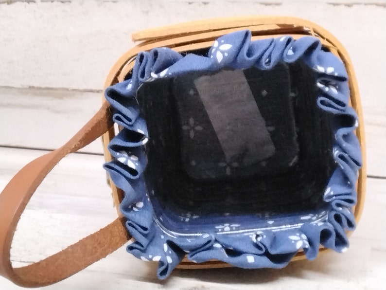 May include: A small, brown wicker basket with a blue fabric lining and a brown leather handle. The fabric lining has a white floral pattern.