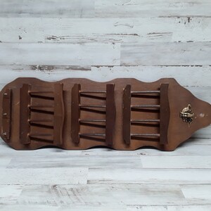 May include: A vintage wooden spice rack with a dark brown finish. The rack features multiple shelves and a decorative brass accent. The rack is designed to hold spice jars and is mounted on a wooden board.
