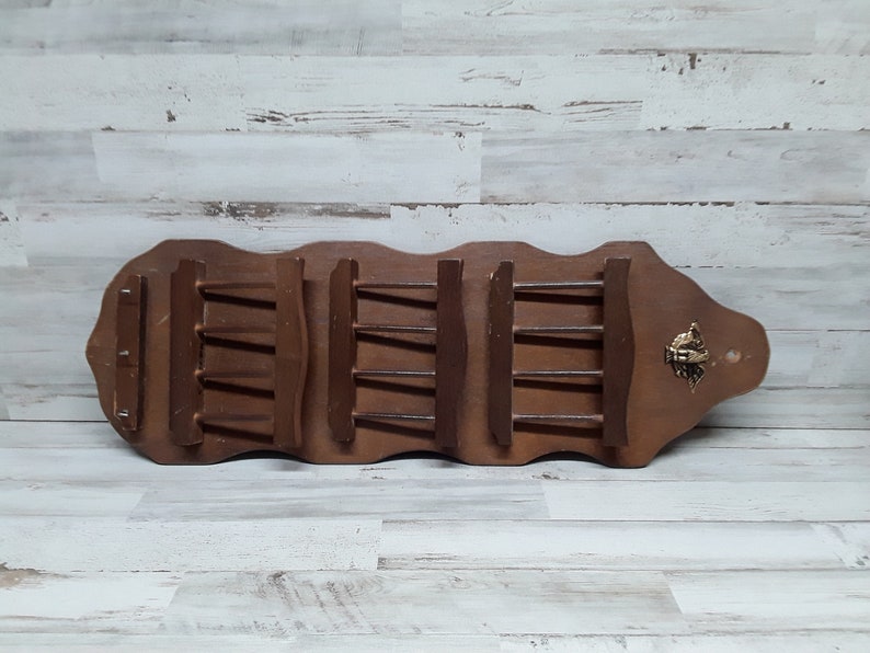 May include: A vintage wooden spice rack with a dark brown finish. The rack features multiple shelves and a decorative brass accent. The rack is designed to hold spice jars and is mounted on a wooden board.