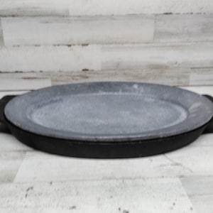 May include: Oval grey stone serving platter with a black cast iron base. The platter has two integrated handles. The serving dish is suitable for presenting appetizers, entrees, or desserts. The dimensions are approximately 30 cm long and 20 cm wide.