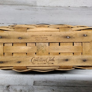 May include: Handwoven rectangular basket with a light brown finish. The bottom of the basket features the text "Longaberger Baskets Handwoven Dresden, Ohio USA" and "Collectors Club 1997 Collectors Edition". The basket is made of woven wood strips.