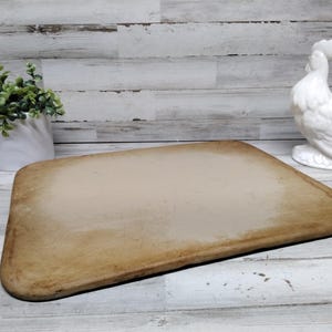 May include: A rectangular baking stone with rounded corners and a smooth, light tan surface. The stone features a slightly darker, weathered border around the edges, indicating previous use. The surface is flat and uniform in texture.