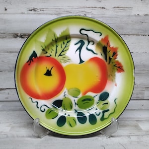 Peut inclure: Une assiette en &eacute;mail vert avec un centre blanc et un motif peint de fruits. Les fruits comprennent deux p&ecirc;ches jaunes et orange et des raisins verts. L'assiette a un bord noir.