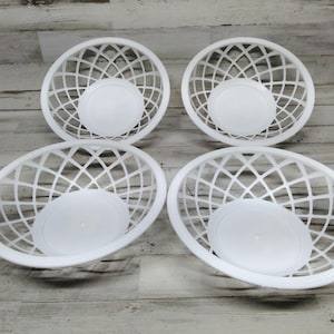 Op de afbeelding: Vier witte ovale plastic manden met een roosterontwerp. Elke mand heeft een effen, ronde bodem. De manden zijn gerangschikt op een lichtgekleurd houten oppervlak.