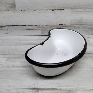 May include: White enamel kidney dish with a black rim. The dish is slightly chipped on the edge.
