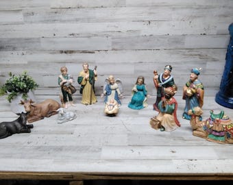 Pode incluir: Um presépio de cerâmica com figuras de Maria, José, o menino Jesus, anjos e os três reis magos. As figuras são pintadas em várias cores, incluindo azul, dourado e verde. Uma vaca, um burro e um cordeiro também estão incluídos.