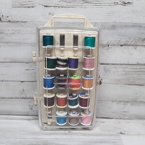 May include: A clear plastic storage box with a white lid and handle. The box is filled with spools of colorful thread.