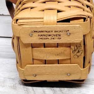 May include: A small, natural-colored, woven basket with a label that reads "Longaberger Baskets Handwoven Dresden Ohio USA".