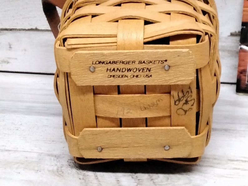 May include: A small, natural-colored, woven basket with a label that reads "Longaberger Baskets Handwoven Dresden Ohio USA".