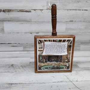 May include: A wooden kitchen prayer box with a brown handle. The box has a white tile with a picture of a kitchen and a prayer that reads "Lord of our past and present and future, grant that I may not be too busy to have time for the things that really matter.  I am so prone to rush through the things that matter most, or to snatch a hasty meal.  There are so many things I want to do, so many places I want to go, so many people I want to see.  Help me to remember that the most important things are the people I love, the things that make me laugh, and the moments that make me feel alive.  Help me to slow down and enjoy the simple things in life.  The kitchen is the heart of the home, and it is here I would like to find the peace and joy that I need.  Amen."