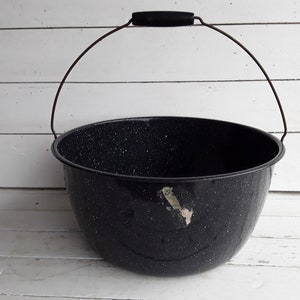 May include: A large black enamelware pot with a speckled finish and a wire handle with a wooden grip.