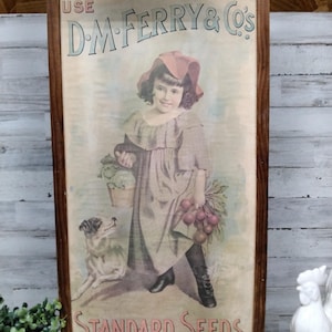 May include: Vintage framed advertisement for D.M. Ferry & Co.'s Standard Seeds. The artwork features a young girl in a dress and hat, holding vegetables and a basket, with a dog at her side. The frame is made of dark wood.