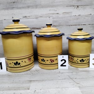 May include: Set of three yellow ceramic canisters with blue and gold trim and floral designs. The canisters are labeled 1, 2, and 3.