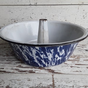 Könnte beinhalten: Vintage Gugelhupf-Form aus Emaille mit blau-weißem Wirbelmuster. Die Form hat einen Mittelrohr und einen schwarzen Rand. Der Innenraum ist weiß. Ein rustikales Küchenutensil.