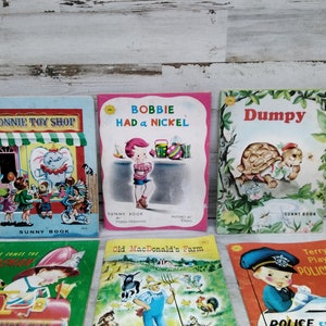 Puede incluir: Una colección de libros infantiles antiguos con ilustraciones coloridas. Los títulos incluyen "Bonnie Toy Shop", "Bobbie Had a Nickel" y "Dumpy". Los libros presentan imágenes de una juguetería, una niña y una tortuga.