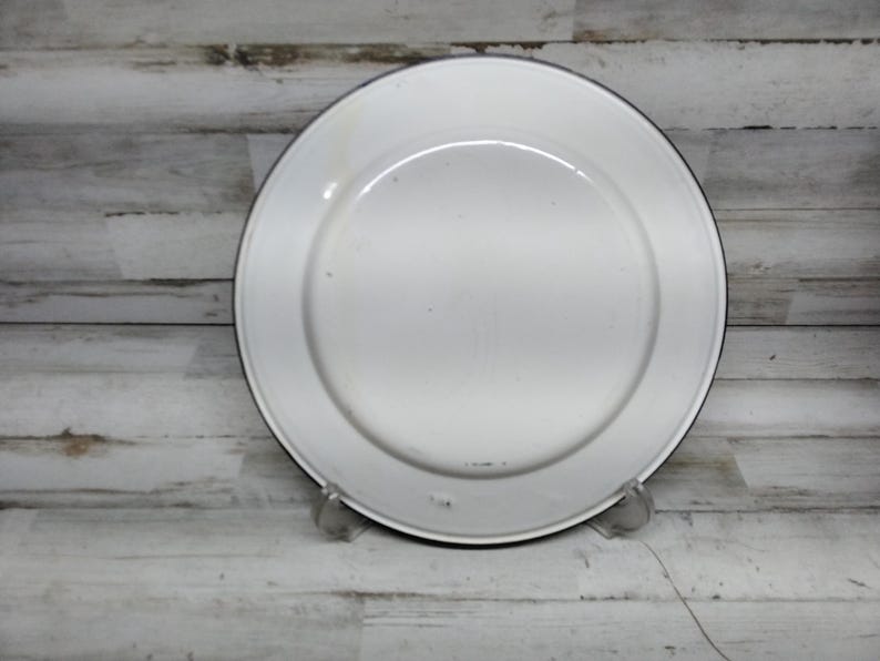 Peut inclure: Assiette en &eacute;mail blanc avec un bord noir. L'assiette est l&eacute;g&egrave;rement us&eacute;e et pr&eacute;sente quelques petites rayures.