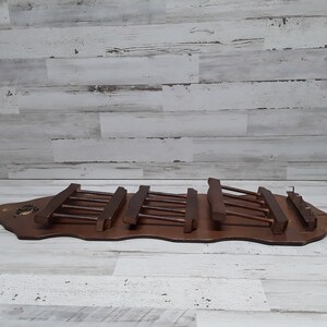 May include: A vintage wooden wall-mounted coat rack with a dark brown finish. The rack features multiple horizontal bars for hanging items. The base is a curved shape with decorative elements.