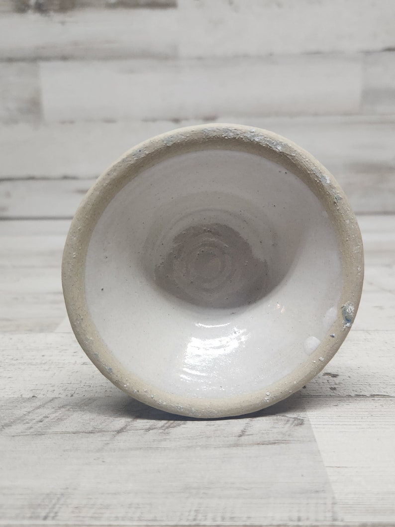 May include: White ceramic bowl with a smooth, glazed interior and a slightly rough, unglazed exterior. The bowl is round and has a wide, shallow shape.