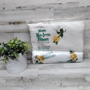 Könnte beinhalten: Weißes, bügelfreies Bettwäsche-Set aus Musselin mit gelbem Rosenblumendesign. Die Verpackung trägt die Aufschrift "50% Polyester, 50% Baumwolle" und "Selected Irregulars". Ein kleiner weißer Topf mit grünen Pflanzen befindet sich im Vordergrund.