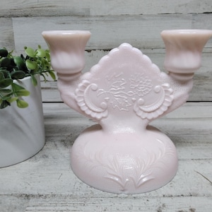 Può includere: Un portacandele vintage in vetro rosa con due portacandele. Il portacandele ha un design decorativo floreale e a foglie. La base è rotonda e il design generale è ornato. Il portacandele è realizzato in vetro rosa chiaro.