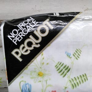 K&ouml;nnte beinhalten: Eine Packung wei&szlig;en Perkalstoffs mit floralem Muster. Die Packung hat ein schwarzes Etikett mit den wei&szlig;en Worten "NO-IRON PERCALE PEQUOT". Das florale Muster umfasst G&auml;nsebl&uuml;mchen, Glockenblumen und gr&uuml;ne Bl&auml;tter.