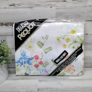 K&ouml;nnte beinhalten: Ein verpacktes Doppel-Flachbettlaken von Pequot mit einem Blumenmuster in Blau, Gelb, Rosa und Gr&uuml;n auf wei&szlig;em Hintergrund. Die Verpackung enth&auml;lt den Text "No-Iron Percale" und "Double Flat Sheet". Das Laken ist f&uuml;r eine Matratze von 137x193 cm.