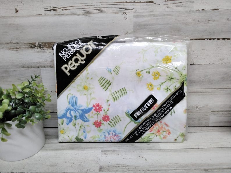 K&ouml;nnte beinhalten: Ein verpacktes Doppel-Flachbettlaken von Pequot mit einem Blumenmuster in Blau, Gelb, Rosa und Gr&uuml;n auf wei&szlig;em Hintergrund. Die Verpackung enth&auml;lt den Text "No-Iron Percale" und "Double Flat Sheet". Das Laken ist f&uuml;r eine Matratze von 137x193 cm.