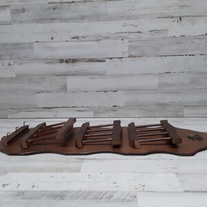 May include: A wooden wine glass rack with a dark brown finish. The rack has a long, curved base with multiple slots for holding wine glasses. The rack is designed to be mounted on a wall.