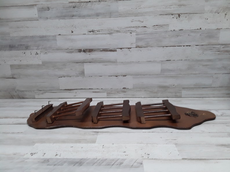 May include: A wooden wine glass rack with a dark brown finish. The rack has a long, curved base with multiple slots for holding wine glasses. The rack is designed to be mounted on a wall.